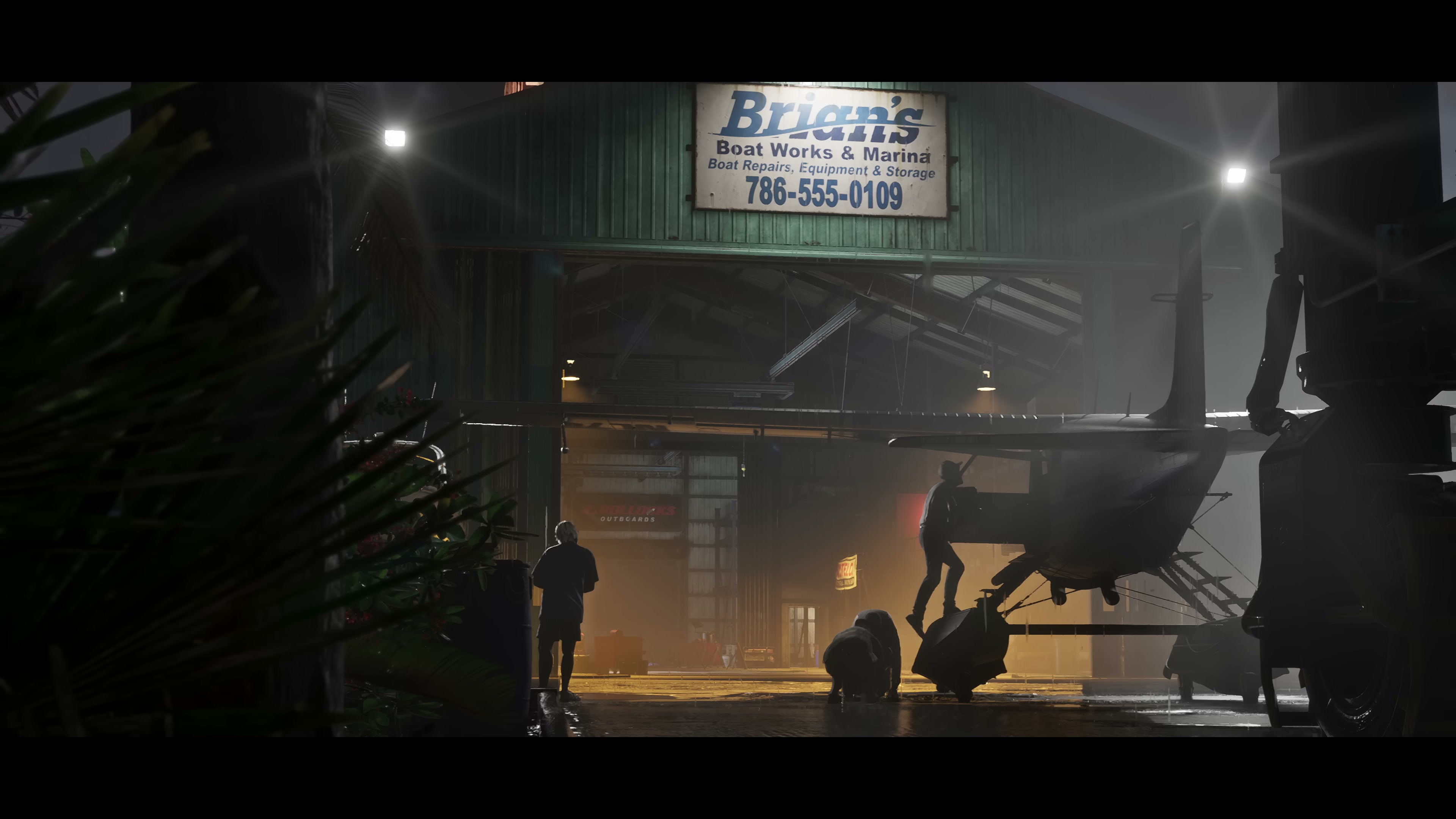 Night-time boat-works hangar with silhouetted figures working under an illuminated sign
